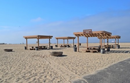 Four of the Brookhurst Berm Ramada sit on the sand next to the paved wheelchair accessible spencer ramp located near our Brookhurst Street entrance. Each ramada has two picnic tables and a fire pit adjacent to it.